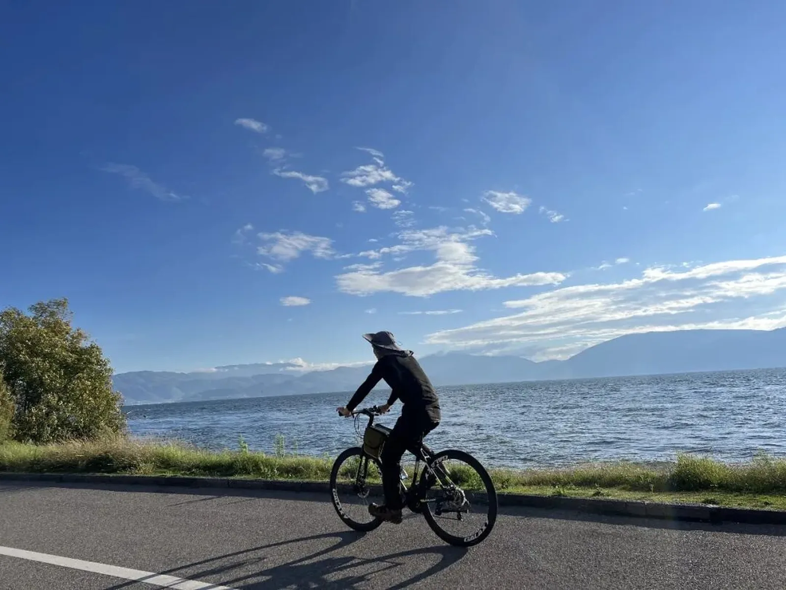 A cyclist riding beside Erhai Lake beneath a wide blue sky